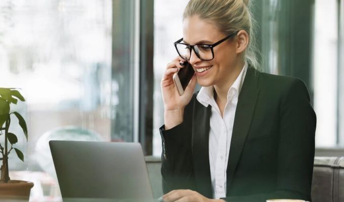 Zdjęcie wizerunkowe, Pani rozmawia przez telefon, uśmiecha się, spogląda w laptopa