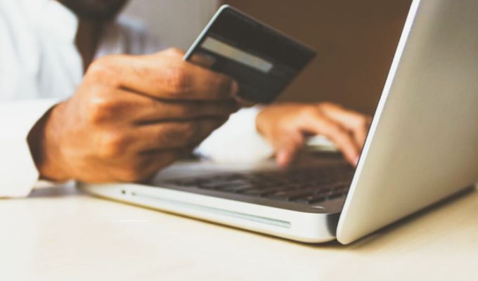 Obrazek dekoracyjny: ktoś trzyma kartę płatniczą w ręku i wpisuje cos do laptopa